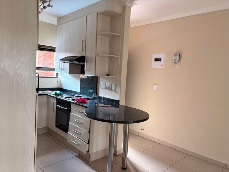 Compact kitchen featuring light wood cabinetry, granite countertops, integrated oven and stove, and a convenient breakfast bar, finished with neutral floor tiles.