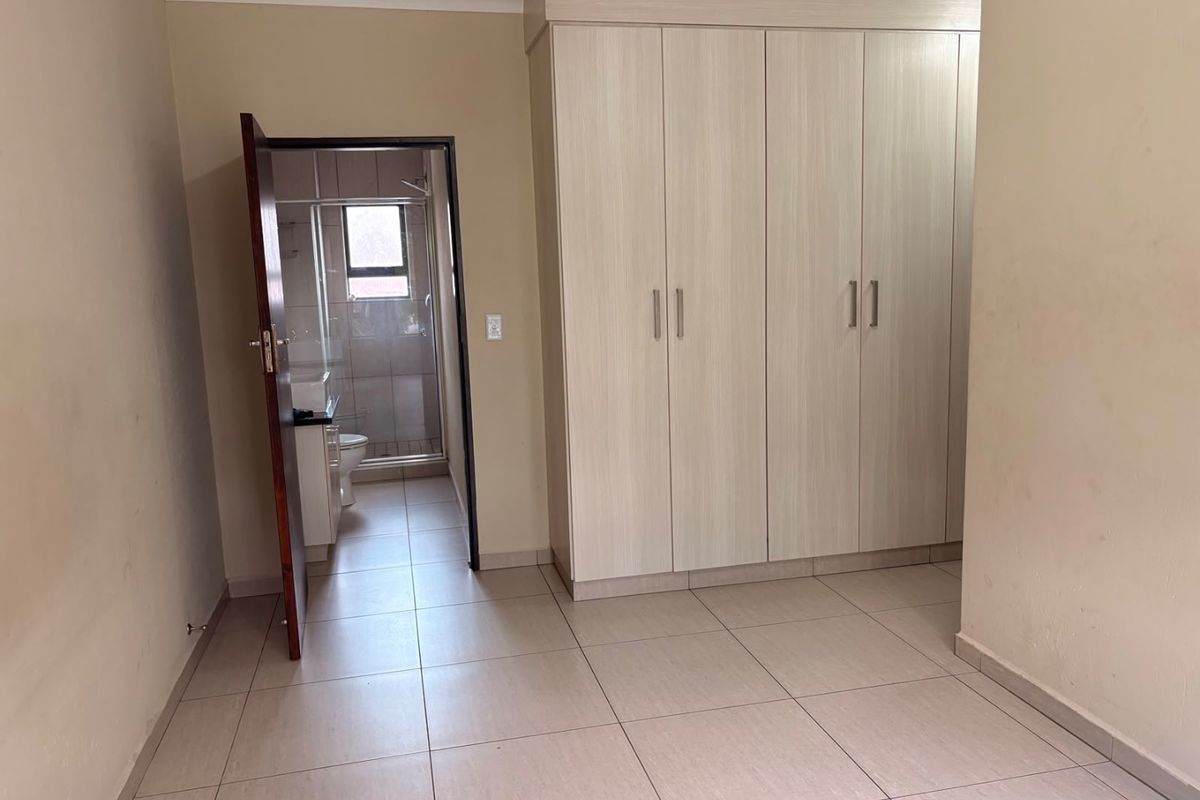 A clean, empty bedroom featuring neutral tiled flooring and ample built-in cupboard space, with direct access to an en-suite bathroom.
