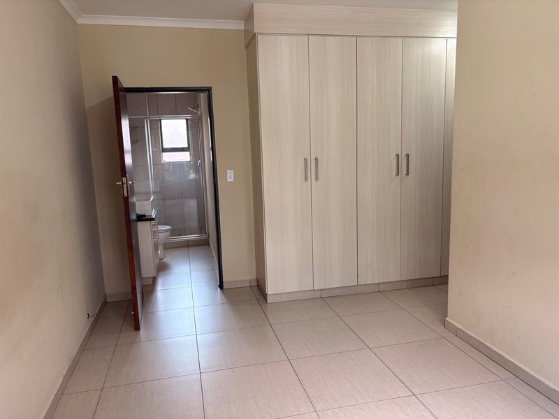 A clean, empty bedroom featuring neutral tiled flooring and ample built-in cupboard space, with direct access to an en-suite bathroom.