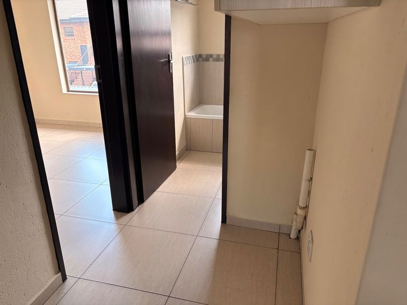 A functional hallway area featuring tiled flooring and visible plumbing connections, providing access to adjacent rooms within the apartment.