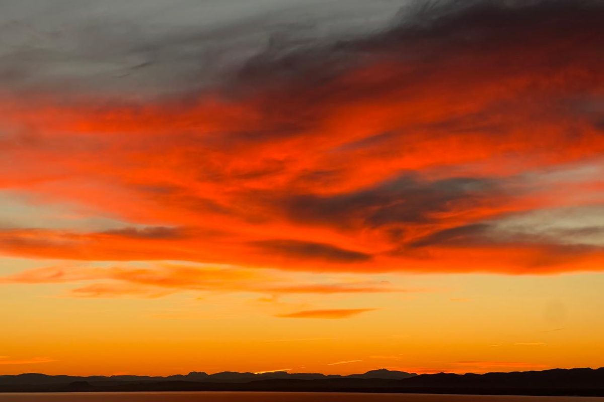 A scenic view of a vibrant sunset over a distant mountain range and water horizon.