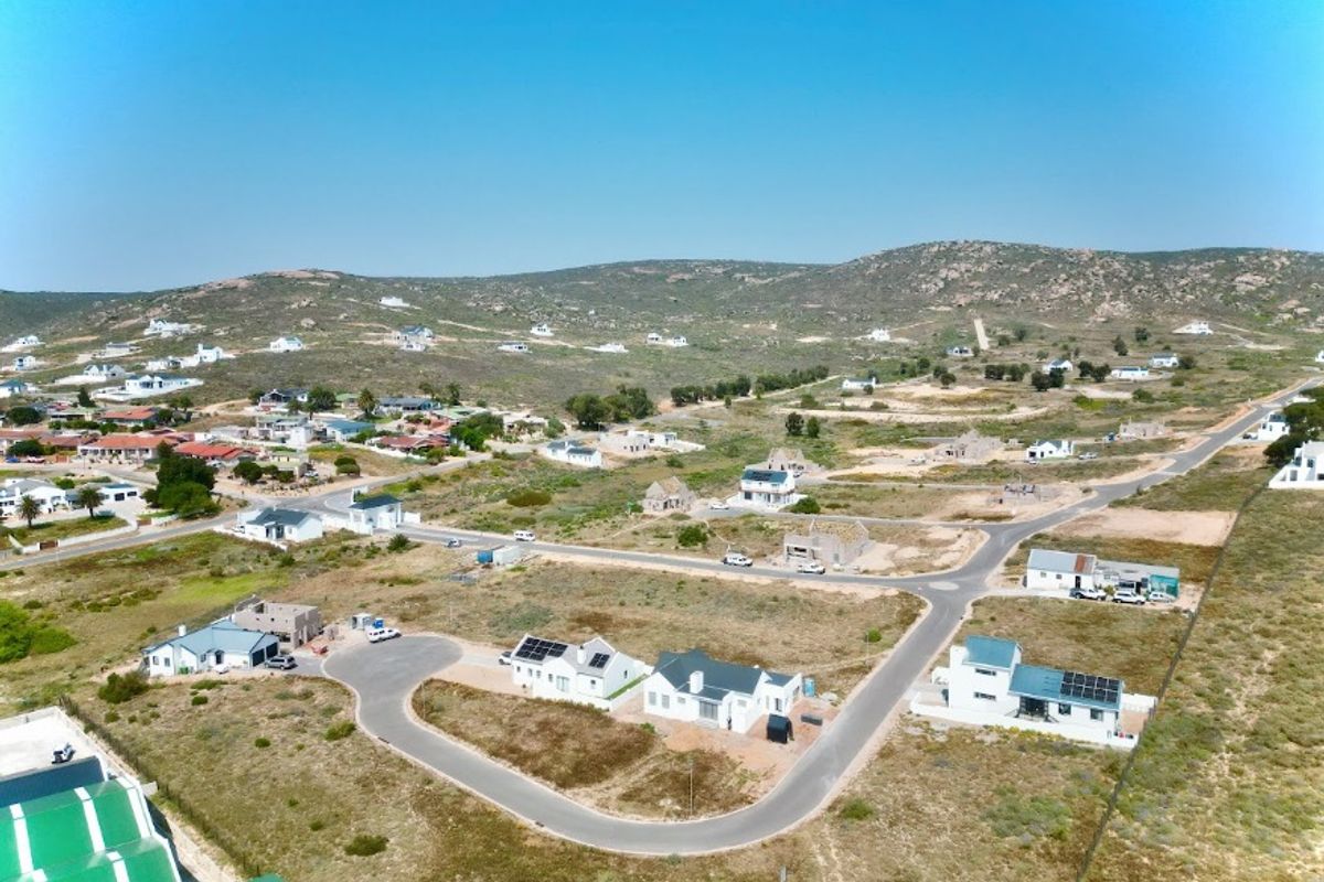 An aerial view of a residential development featuring paved roads, scattered houses, and surrounding natural landscape.