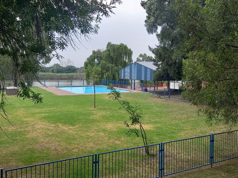 A communal outdoor area featuring a swimming pool, a covered structure, and a large lawn enclosed by metal fencing.