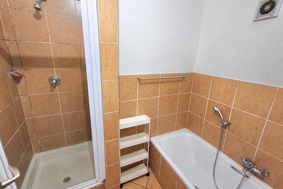 A functional bathroom featuring a separate shower enclosure, a bathtub with a handheld shower mixer, and neutral ceramic tiling throughout.