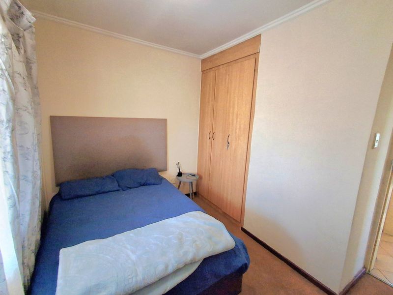 A functional bedroom featuring a built-in wooden wardrobe and neutral wall finishes, providing a practical and comfortable sleeping space.