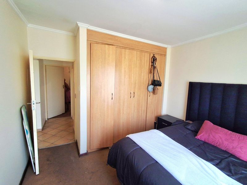 A bedroom featuring a built-in wooden wardrobe, carpeted flooring, and a coved ceiling, with an adjacent hallway visible through the doorway.