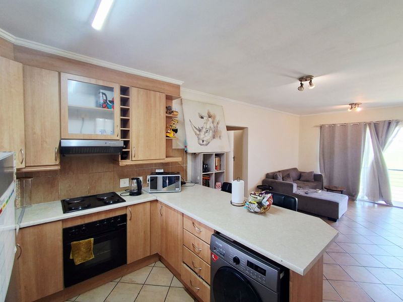 Open-plan kitchen and living area featuring light wood cabinetry, built-in appliances, tiled flooring, and direct access to a balcony.