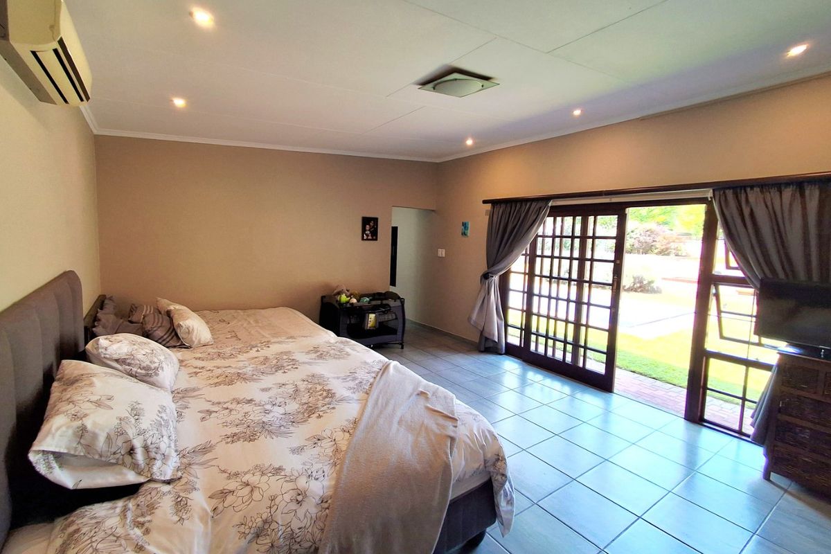 Spacious bedroom featuring tiled flooring, recessed lighting, a wall-mounted air conditioner, and large sliding glass doors providing direct access to the garden.