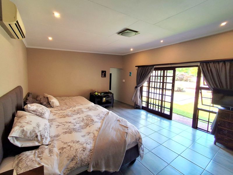 Spacious bedroom featuring tiled flooring, recessed lighting, a wall-mounted air conditioner, and large sliding glass doors providing direct access to the garden.
