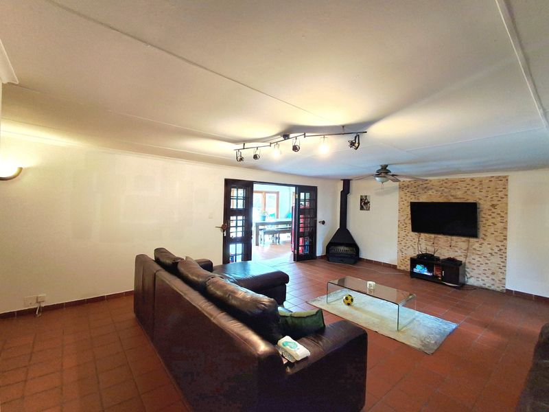 Spacious living room featuring terracotta tile flooring, a stone-clad feature wall with a fireplace, and direct access to an adjoining room via french doors.
