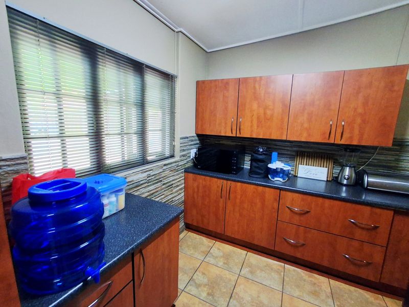A functional kitchen featuring wood-look laminate cabinetry, dark countertops, a textured tiled backsplash, and ceramic floor tiles.