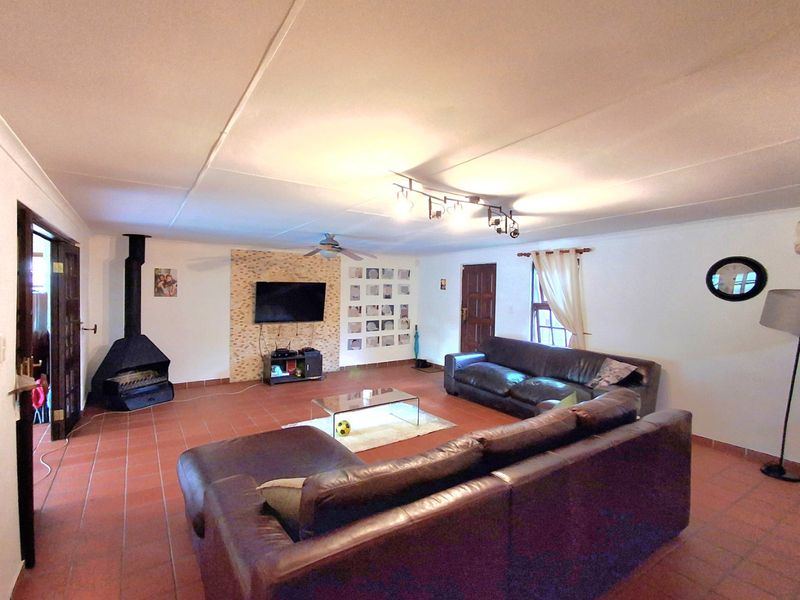 Spacious living room featuring a stone accent wall, a freestanding fireplace, tiled flooring, and a ceiling fan.