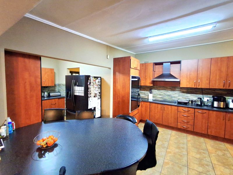 Open-plan kitchen featuring wood-finish cabinetry, laminate countertops, built-in oven, extractor fan, and tiled flooring, seamlessly connected to a dining area.