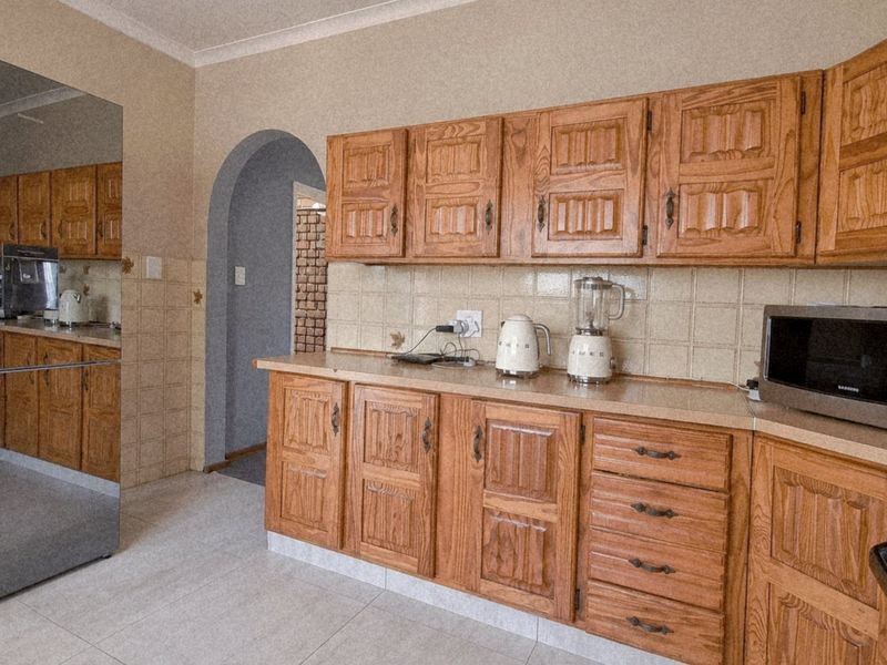 A functional kitchen featuring traditional wooden cabinetry, tiled backsplash, and neutral floor tiles, offering a classic layout with potential for modern updates.