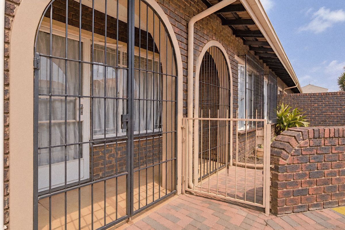 Rear exterior view of the townhouse featuring a paved patio area, brick facade, and secure metal security gates.