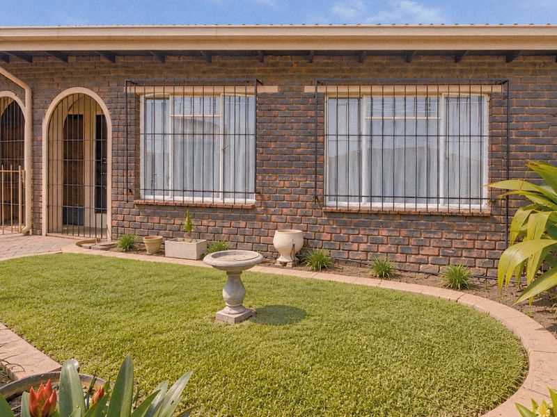 A well-maintained townhouse exterior featuring a face brick facade, arched entrance, security bars on windows, and a neat front garden with a paved walkway.