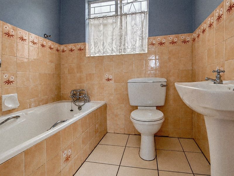 A dated bathroom featuring a bathtub, pedestal basin, and toilet with original tiled finishes and natural light from a window.