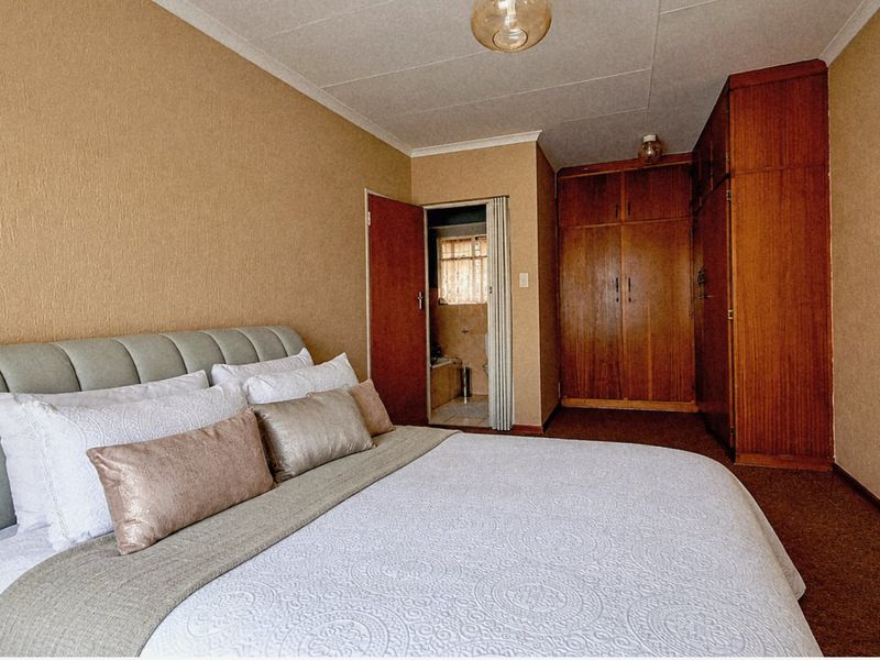 A bedroom featuring built-in wooden cupboards, carpeted flooring, and direct access to an en-suite bathroom.