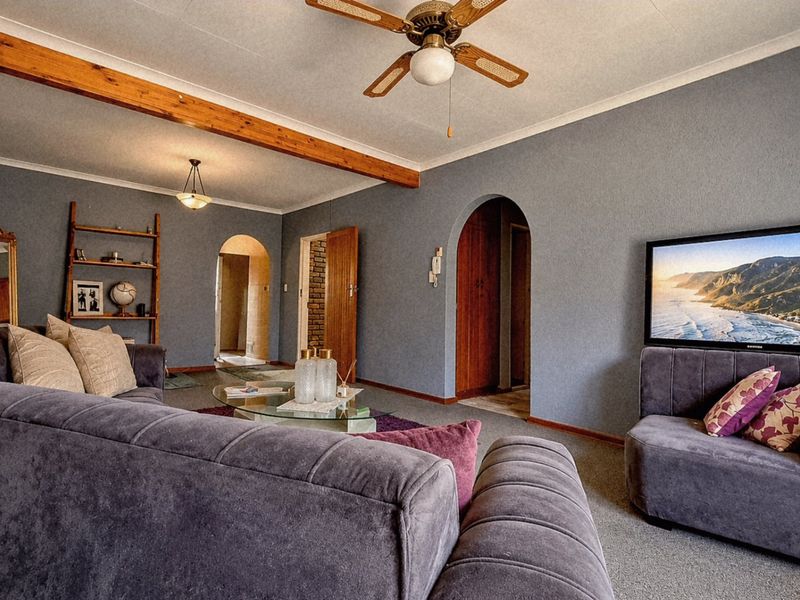 A living room featuring an exposed timber ceiling beam, ceiling fan, and arched doorways leading to adjacent areas, finished with carpeted flooring.
