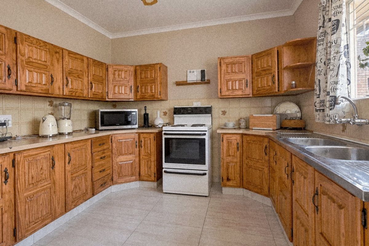 A functional kitchen featuring traditional wooden cabinetry, tiled backsplash, a freestanding oven, and a double stainless steel sink with tiled flooring.