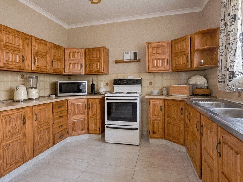A functional kitchen featuring traditional wooden cabinetry, tiled backsplash, a freestanding oven, and a double stainless steel sink with tiled flooring.