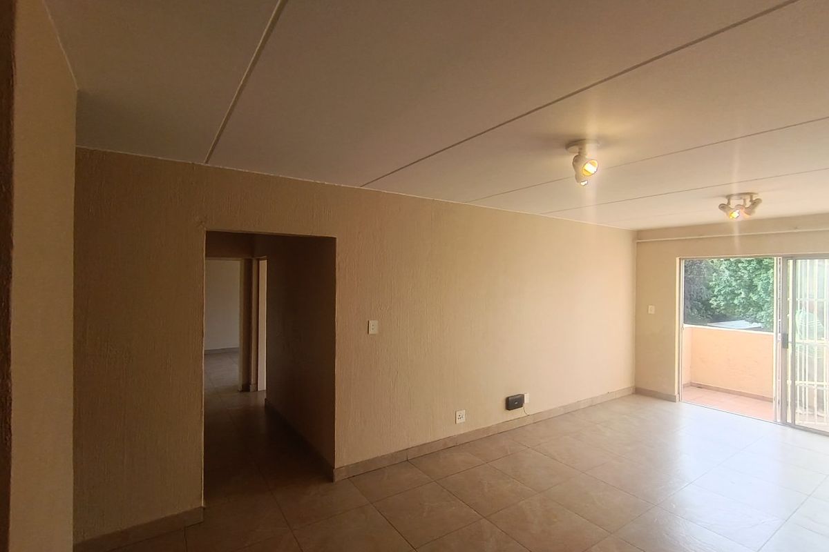 An empty, open-plan living area featuring tiled flooring, textured walls, and a sliding glass door providing access to an outdoor balcony.