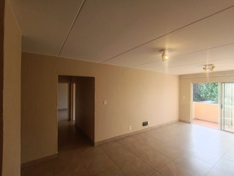 An empty, open-plan living area featuring tiled flooring, textured walls, and a sliding glass door providing access to an outdoor balcony.