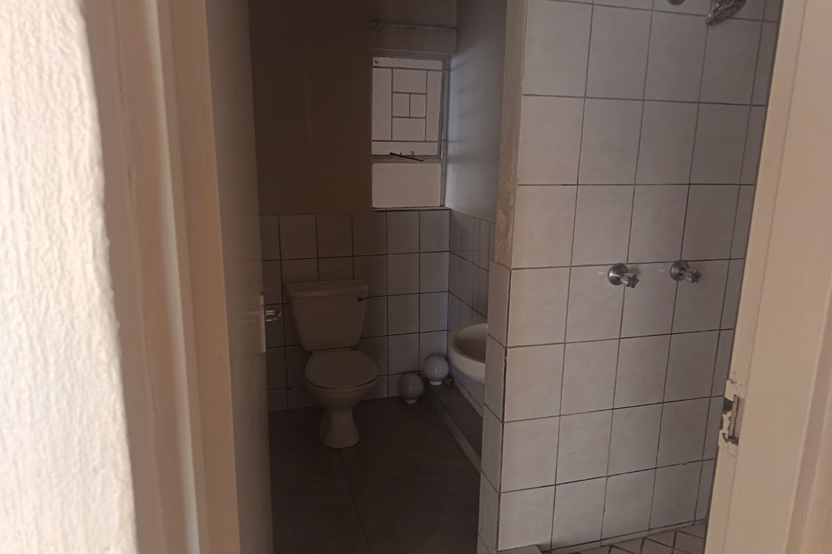 A functional bathroom featuring a shower, toilet, and wash basin with tiled finishes, requiring some cosmetic updates to improve its overall condition.