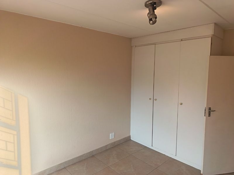 A clean, empty bedroom featuring neutral wall tones, tiled flooring, and built-in storage cupboards.