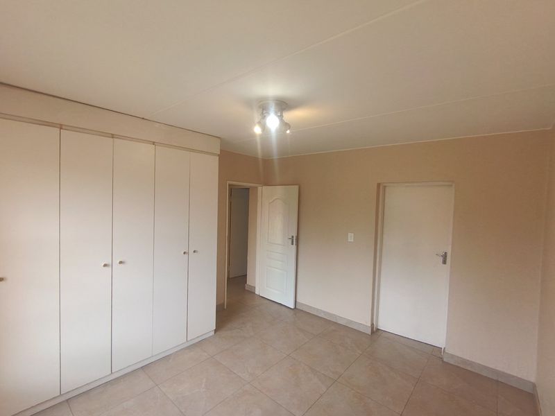 A clean, empty bedroom featuring neutral tiled flooring, built-in cupboards, and standard internal doors, providing a blank canvas for personalization.