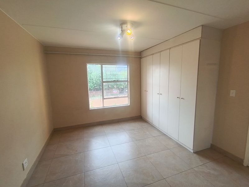 A clean, empty bedroom featuring neutral tiled flooring, built-in cupboards, and a window with security bars, offering a blank canvas for personalization.