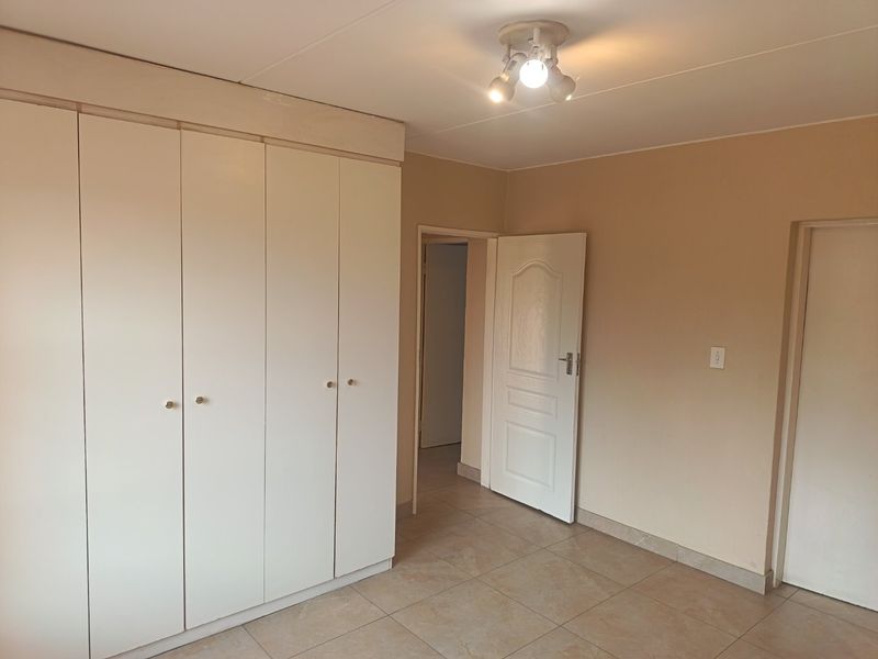 A clean, empty bedroom featuring neutral wall tones, tiled flooring, and ample built-in cupboard storage space.