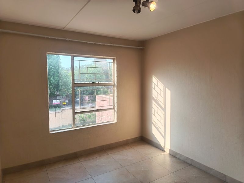 A bright, empty bedroom featuring tiled flooring, security bars on the window, and a ceiling-mounted spotlight fixture.