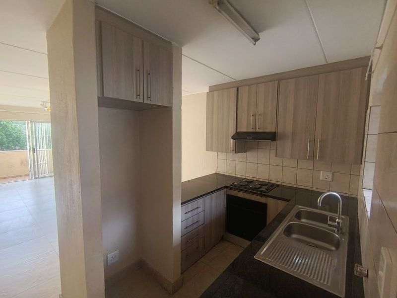 Compact kitchen featuring wood-look cabinetry, granite countertops, built-in oven and hob, and a double bowl sink, offering a functional layout.