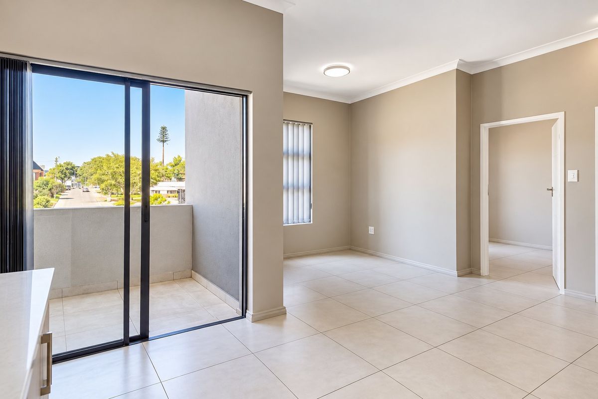An empty, well-lit living area featuring neutral tiled flooring, modern cornice detailing, and a sliding glass door leading to a private balcony.