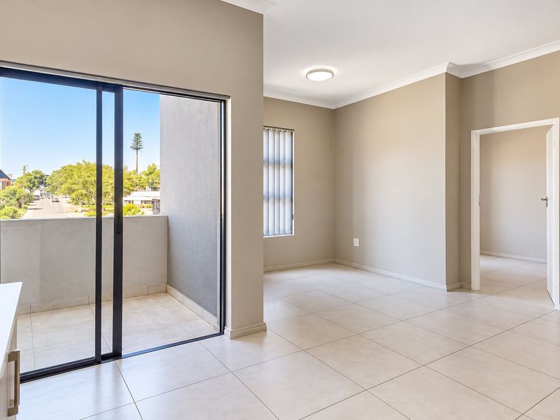 An empty, well-lit living area featuring neutral tiled flooring, modern cornice detailing, and a sliding glass door leading to a private balcony.