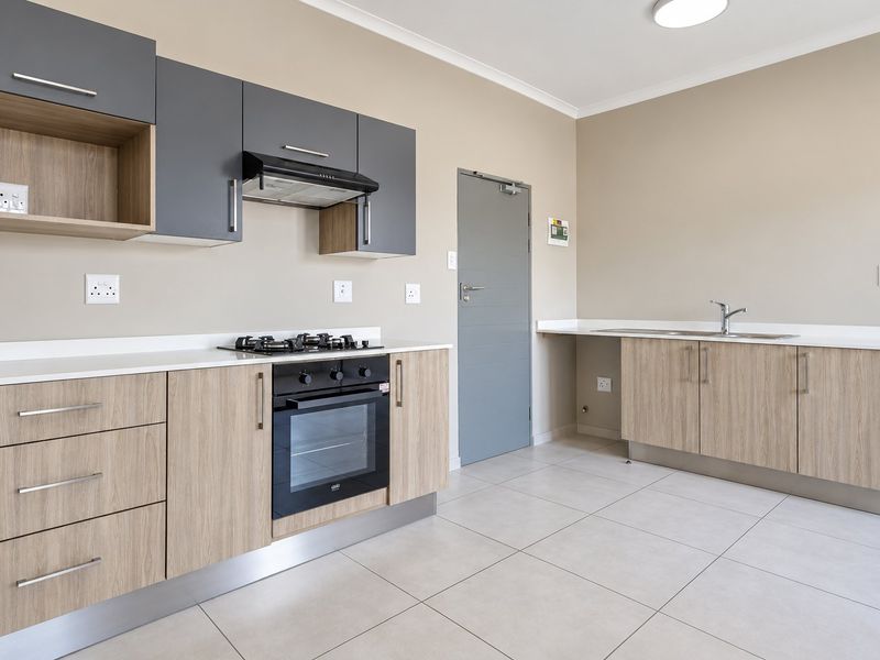 Modern kitchen featuring light wood-grain cabinetry, contrasting grey upper cabinets, stone countertops, built-in gas hob, electric oven, and tiled flooring.