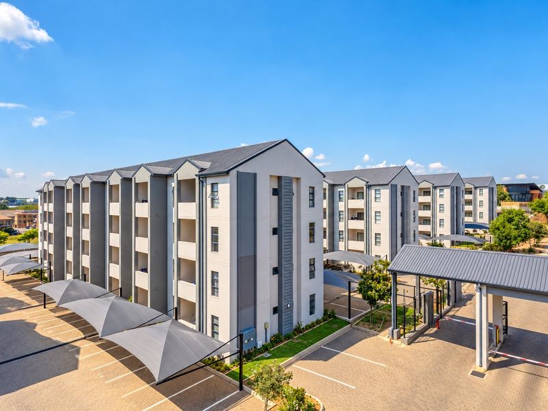 Aerial view of a modern apartment complex featuring paved parking with shade cloth carports, secure access control, and well-maintained multi-story residential buildings.