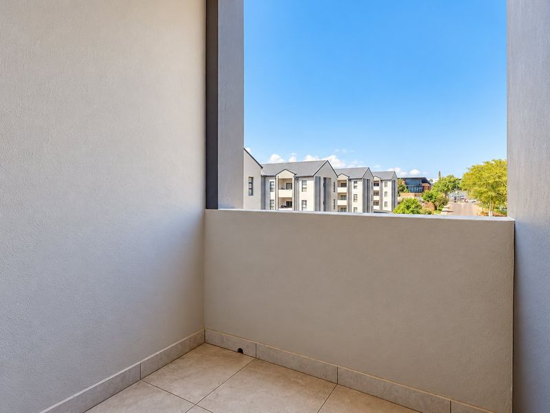 A clean, modern balcony featuring tiled flooring and a solid balustrade, offering an open view of the surrounding apartment complex.
