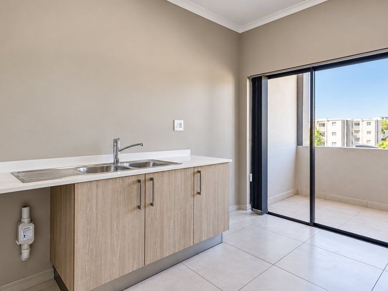 A clean, modern kitchen area featuring light wood cabinetry, a stainless steel sink, and direct access to a private balcony through sliding glass doors.