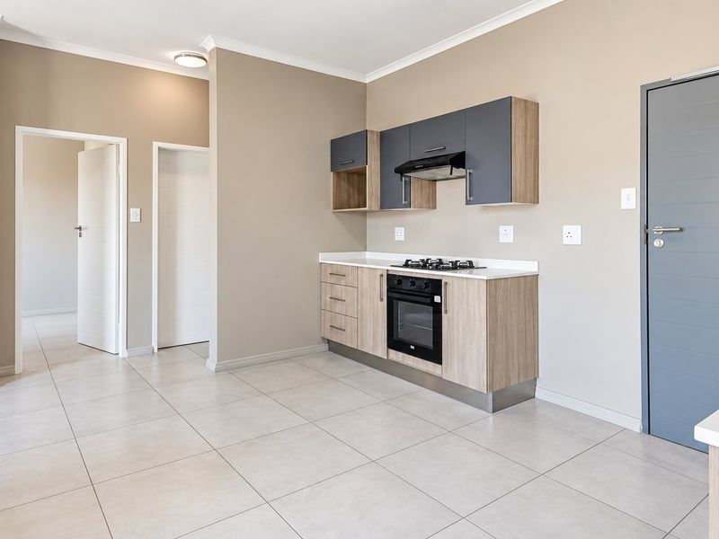 Modern kitchen featuring light wood-tone cabinetry, contrasting grey upper cupboards, built-in oven, gas hob, and sleek tiled flooring in an open-plan layout.