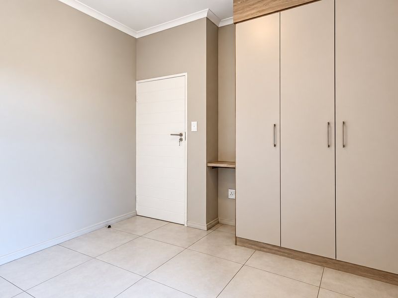 A clean, modern bedroom featuring neutral wall tones, large built-in cupboards with integrated shelving, and light-colored floor tiles.