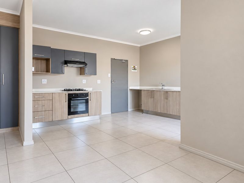 Modern open-plan kitchen featuring two-tone cabinetry, built-in gas hob, electric oven, extractor fan, and tiled flooring in a clean, well-maintained apartment setting.