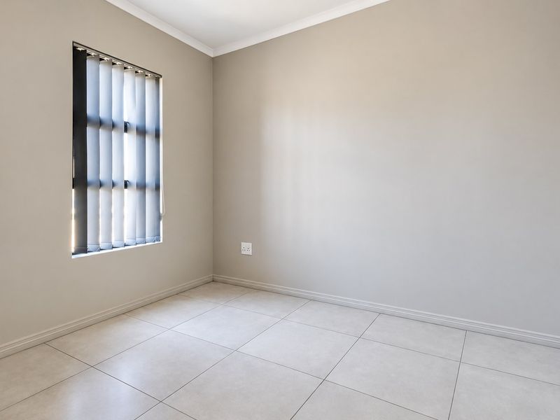 A clean, empty bedroom featuring neutral wall paint, light-colored floor tiles, and vertical window blinds, offering a blank canvas for personalization.