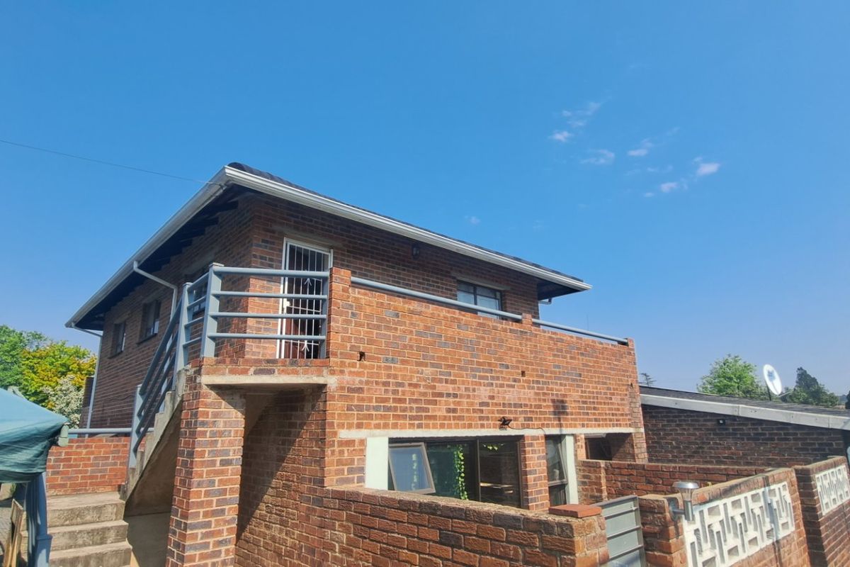 Exterior view of a two-story face brick apartment building featuring an upper-level balcony with metal railings and an external concrete staircase.