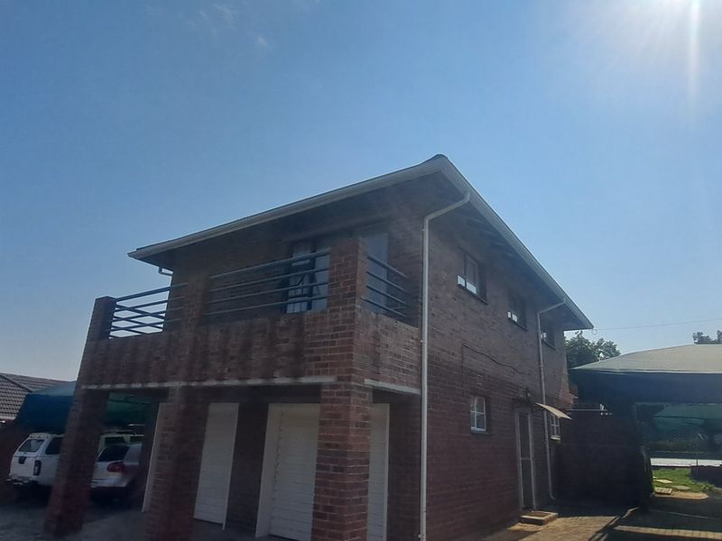 A two-story face brick apartment building featuring a balcony with metal railings and ground-level garage access.