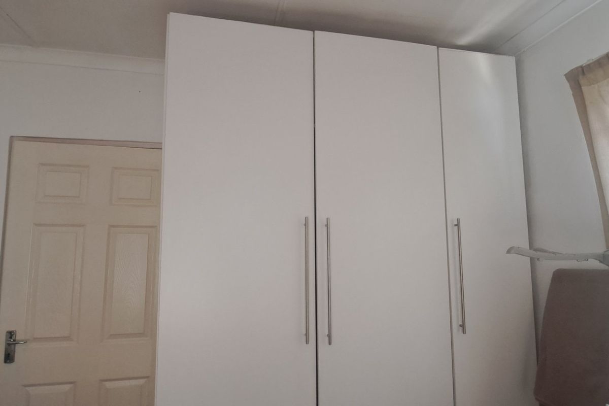 A bedroom featuring a clean, white built-in wardrobe with modern vertical handles and a classic panel door.