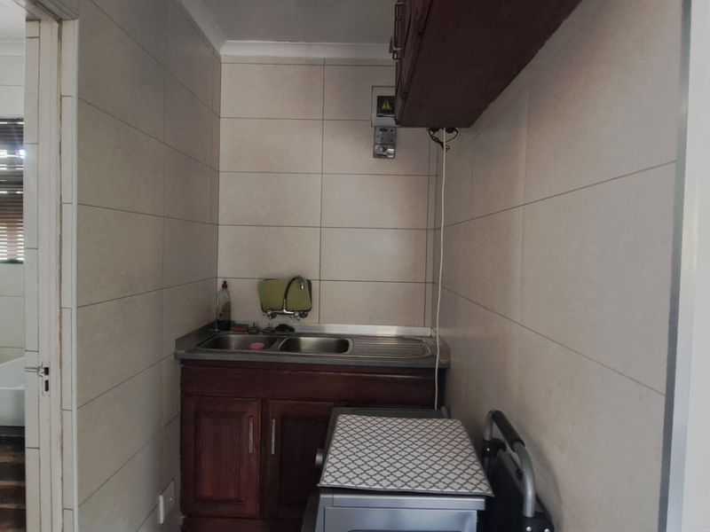 A functional scullery area featuring a double sink, built-in wooden cabinetry, and tiled wall finishes, providing additional utility space adjacent to the bathroom.