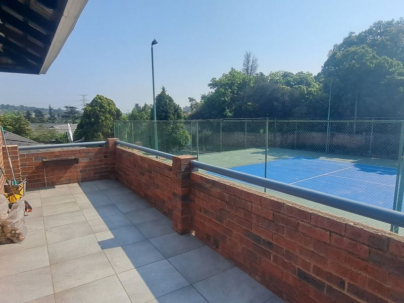 A spacious balcony featuring brick walls and tiled flooring, offering an elevated view overlooking the adjacent tennis court.