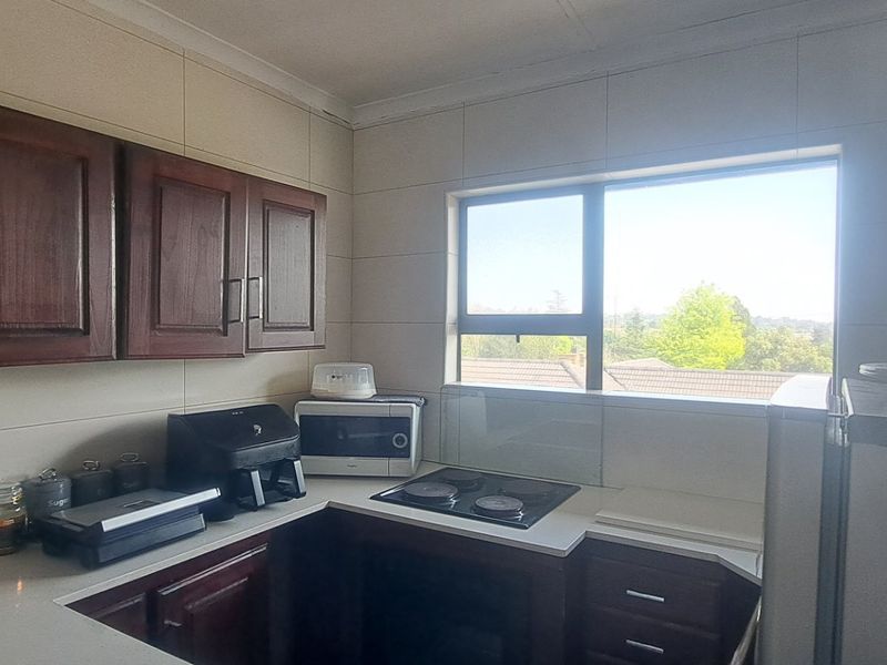 A functional kitchen featuring dark wood cabinetry, stone countertops, a built-in electric hob, and an oven with a tiled backsplash and window view.